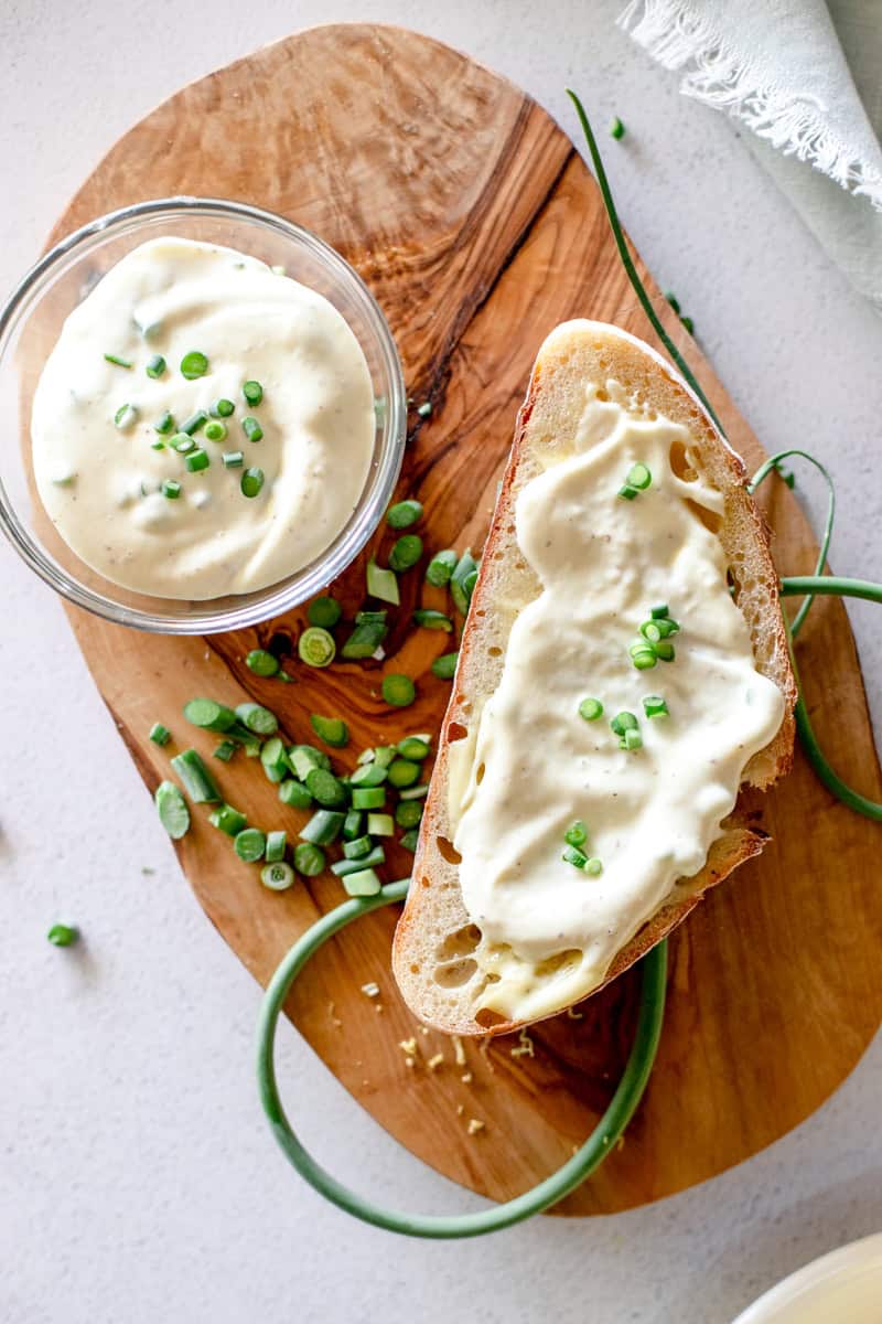 An herbed garlic scape mayo in a glass prep bowl served on a slice of sourdough bread.