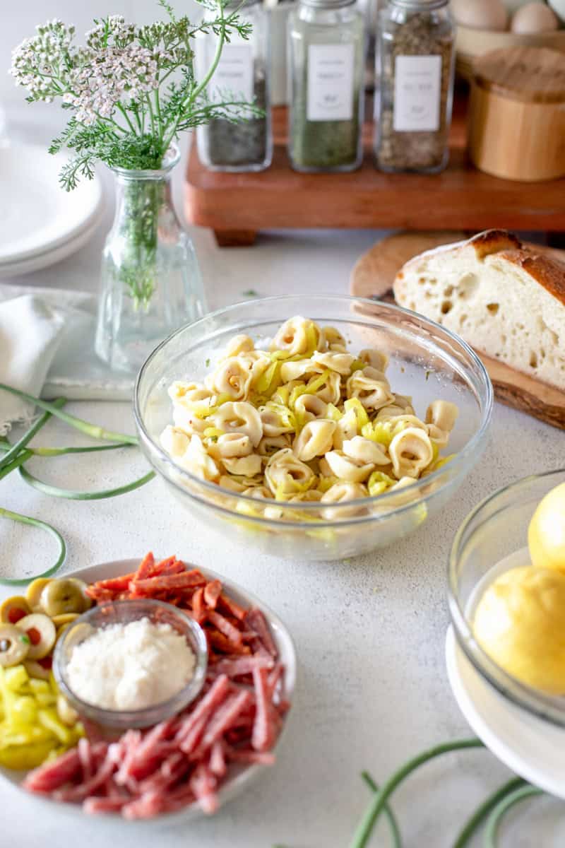 A pasta salad that hasn't been mixed together yet with the ingredients in prep bowls including garden scapes and tortellini.