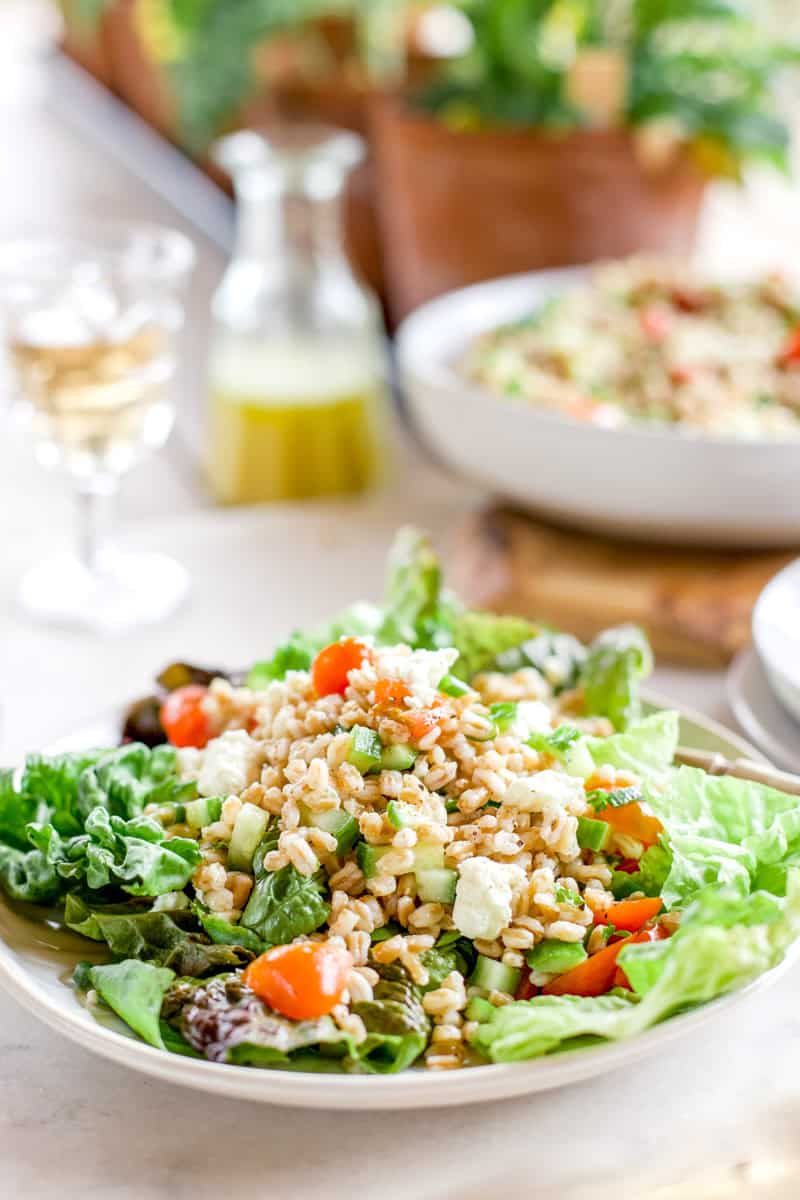 A salad topped with farro and dressed with lemon vinaigrette on a white plate.