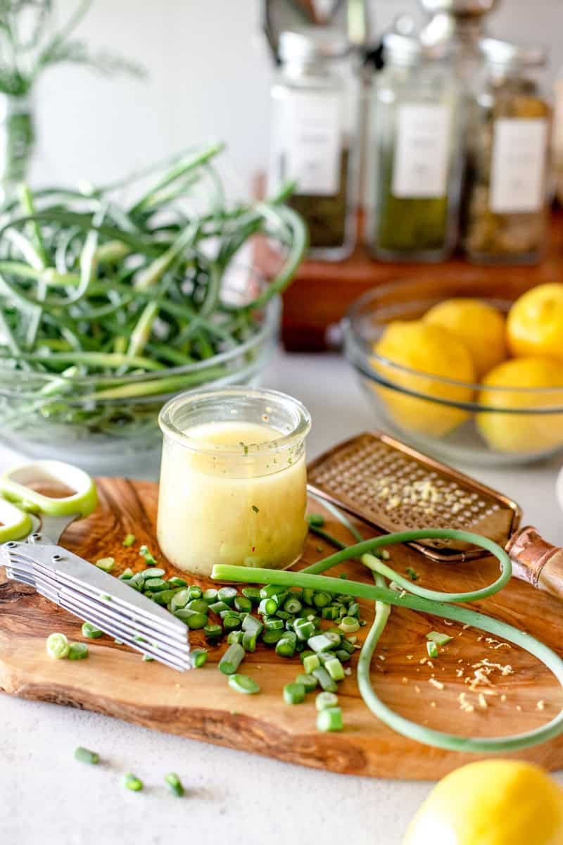 A lemon vinaigrette with garlic scapes in a small glass jar.