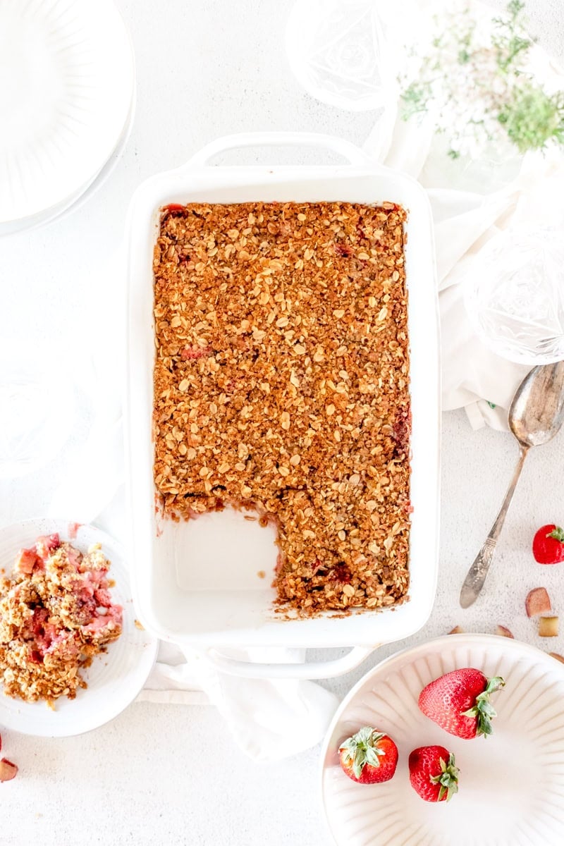 A fruit crisp made with strawberries and rhubarb on a white table garnished with strawberries.
