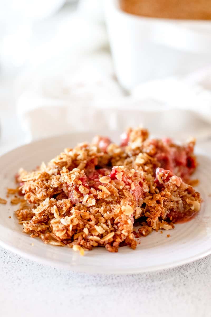A close up view of a strawberry rhubarb crisp that shows the detail of the fruit on a white plate.