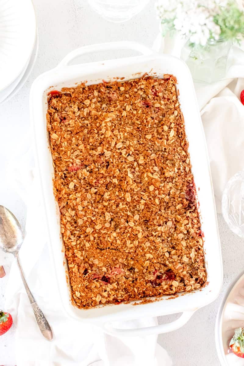 A top view of a strawberry rhubarb crisp, golden brown, in a white baking dish on a white background.
