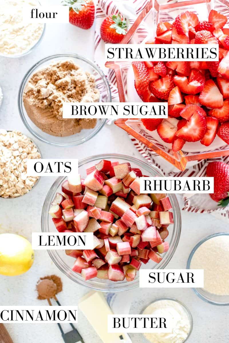 A top view of the ingredients for baking a strawberry rhubarb crisp in little prep bowls on a white background.