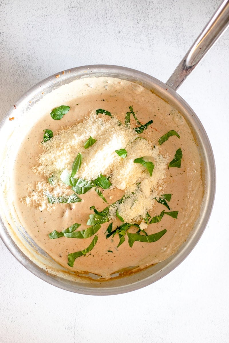 Step 6 of making Loaded Marry Me Chicken pasta is adding the grated parmesan and fresh herbs to the cream sauce.