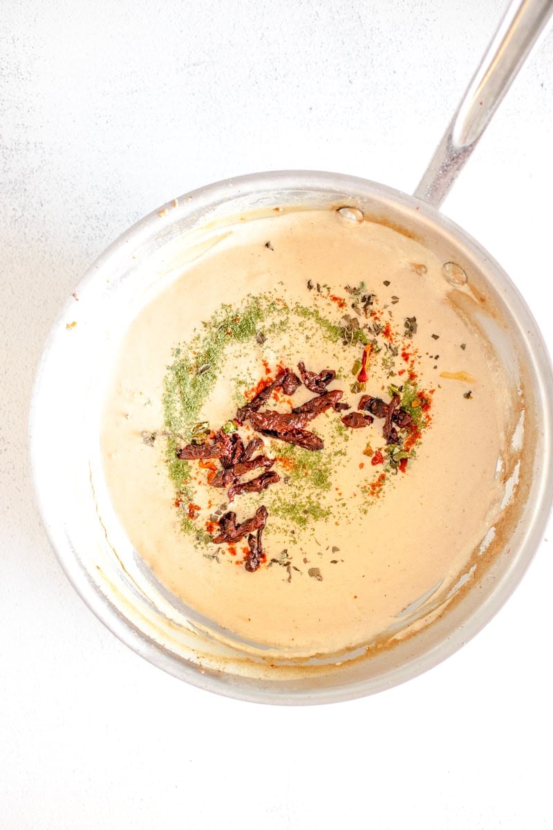 Step 5 of making Loaded Marry Me Chicken pasta is adding the dried tomatoes and herbs to the cream sauce and simmering it.