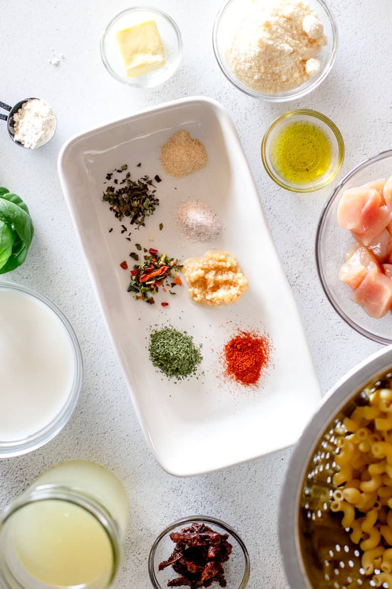 A top view of the ingredients for Loaded Marry Me Chicken Pasta in prep bowls on a white background.