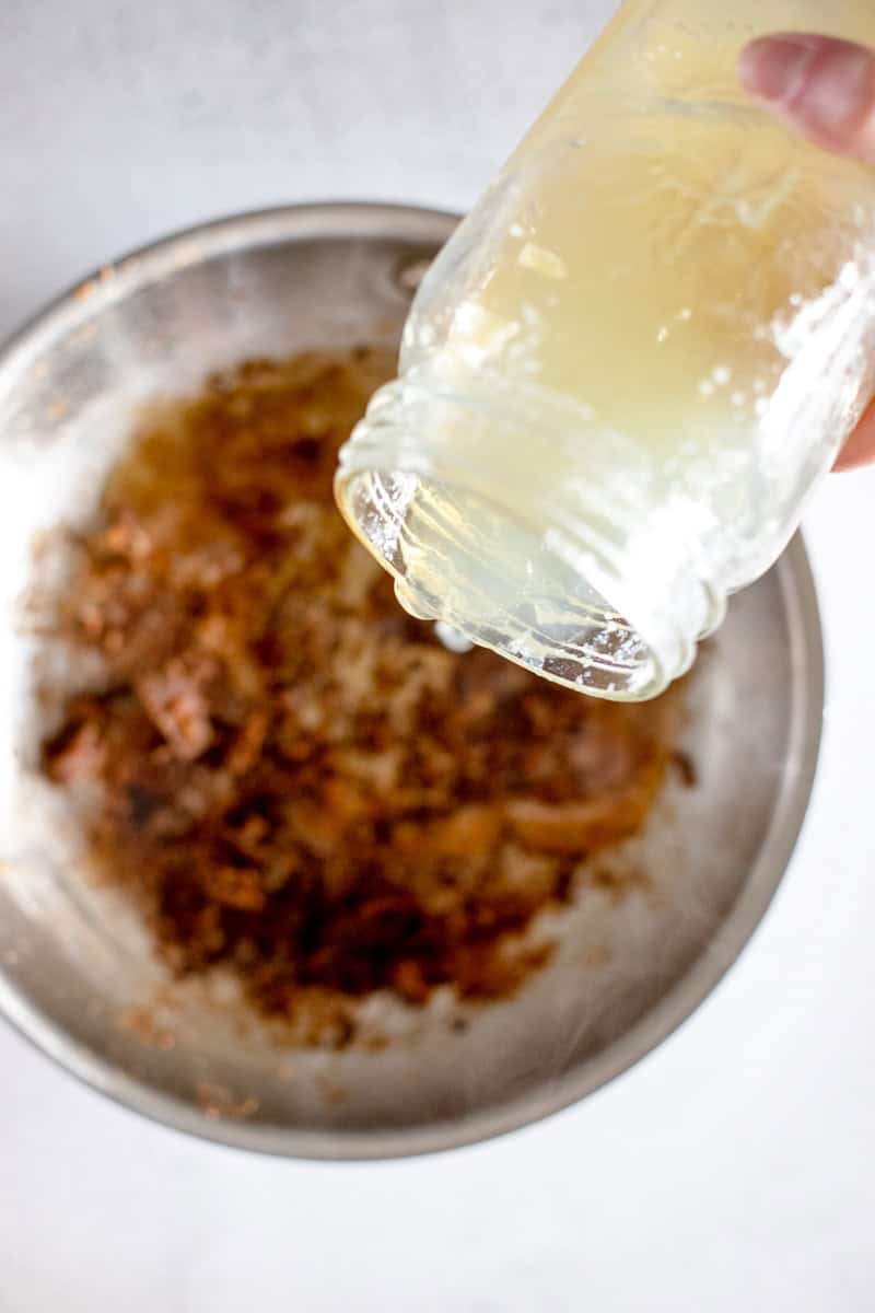 Pouring the chicken broth into the pan of flour, butter and chicken drippings during Step 3 of making Loaded Marry Me Chicken pasta.