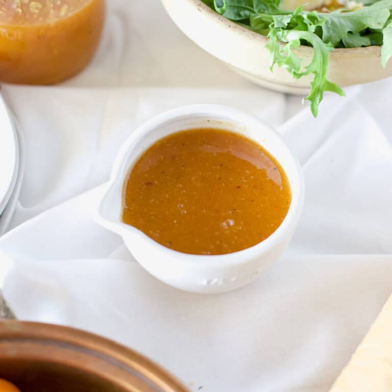 A white mini bowl with pour spout filled with apricot dressing on a white background.