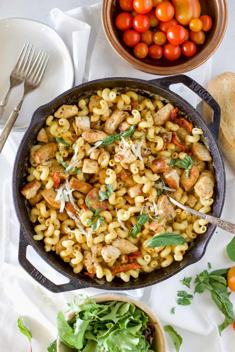 A cast iron skillet filled with Loaded Marry Me Chicken Pasta garnished with cherry tomatoes and fresh basil.