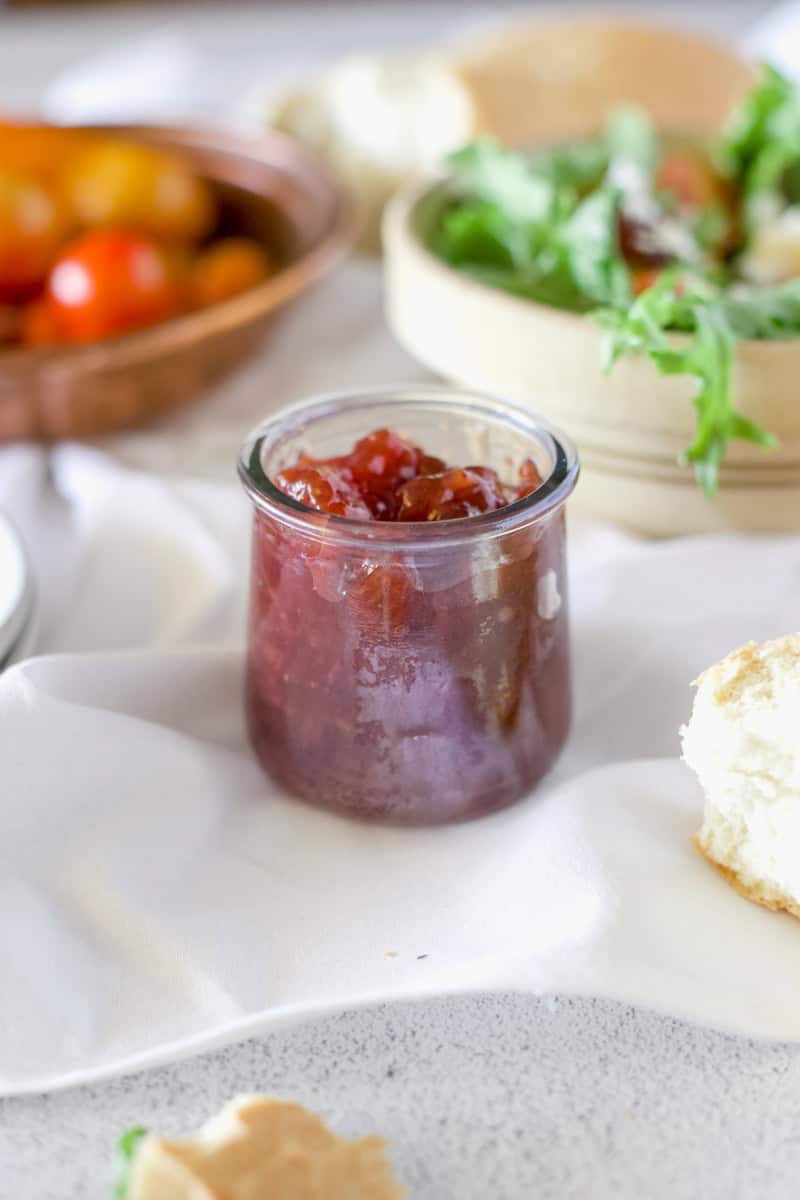 A jar of strawberry preserves surrounded by the ingredients for a Strawberry Preserves Smash Salad With Chicken.