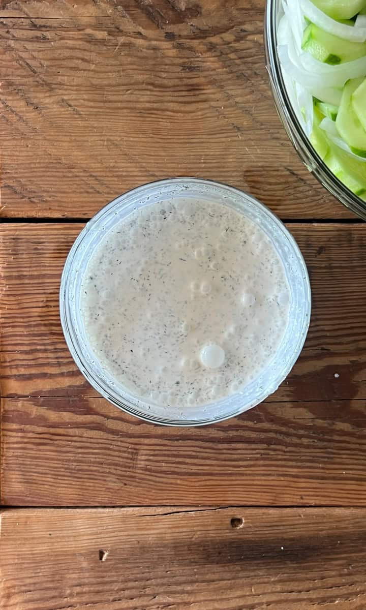 Step two of making a cucumber salad is mixing the dressing by combining the vinegar, salt, pepper and sour cream in a bowl and whisking until smooth.