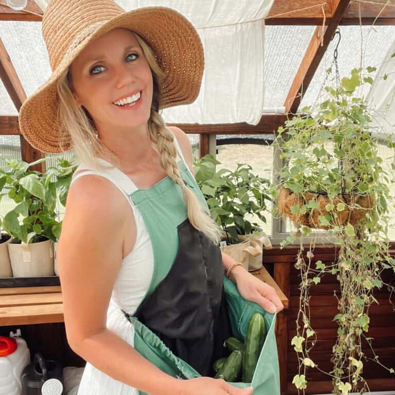A picture of Meg Austin from Ninnescah Homestead in her greenhouse smiling and wearing a roo garden apron.