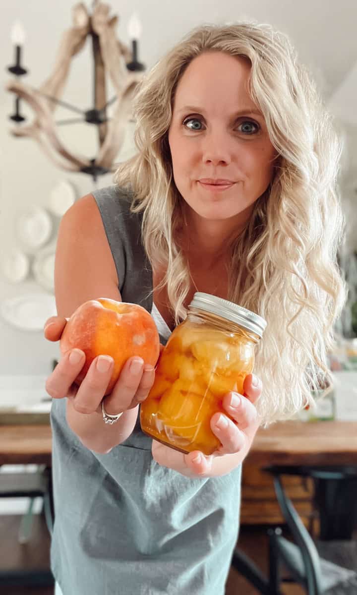 Meg from Ninnescah Homestead holding a jar of peaches and wearing a smock apron.