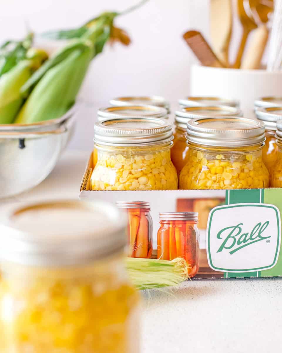 Pressure canned sweet corn packed into ball canning jars and tucked neatly back into the original box.
