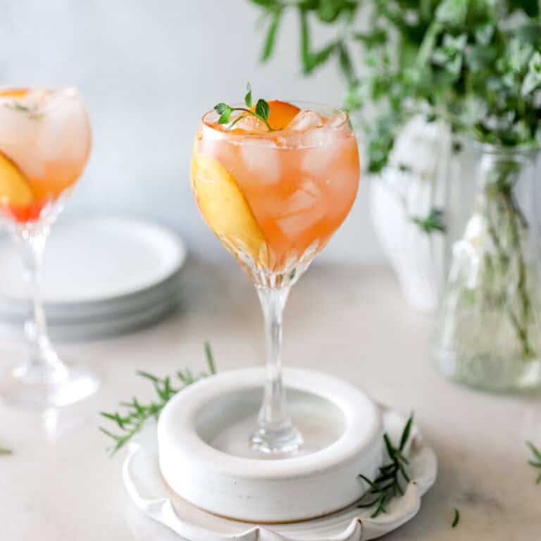 A FRESH PEACH KENTUCKY MULE (BOURBON COCKTAIL RECIPE) in a stemmed glass with garnish of sprigs of mint showing the sunset color of the drink.