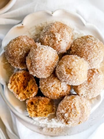 A close up view of pumpkin spice donut holes piled on a white plate.