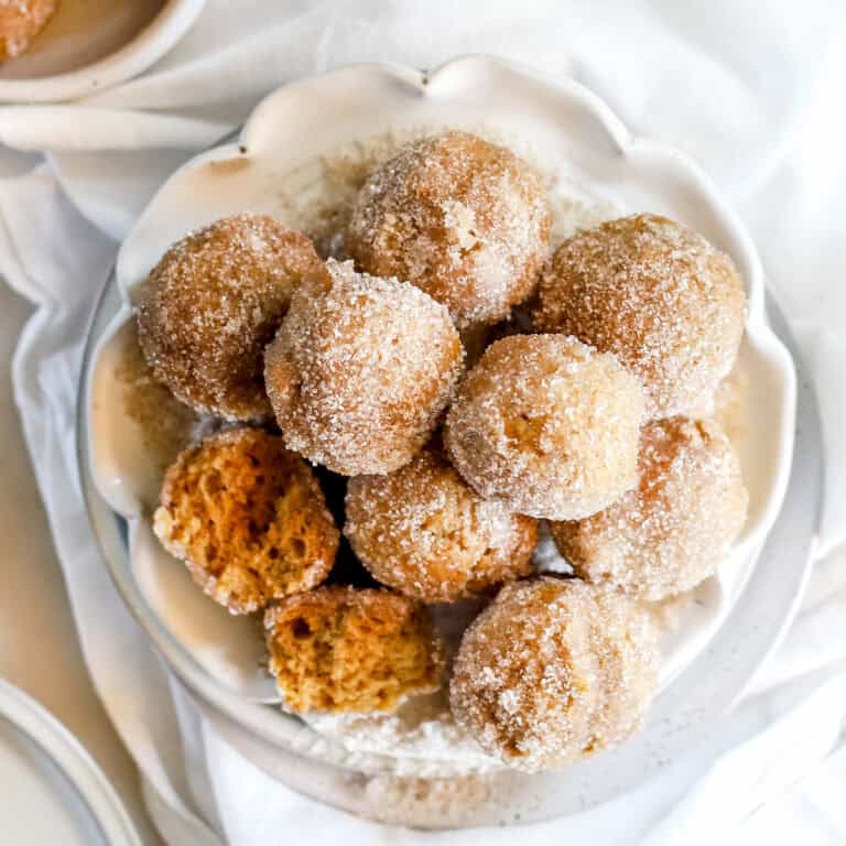 A close up view of pumpkin spice donut holes piled on a white plate.
