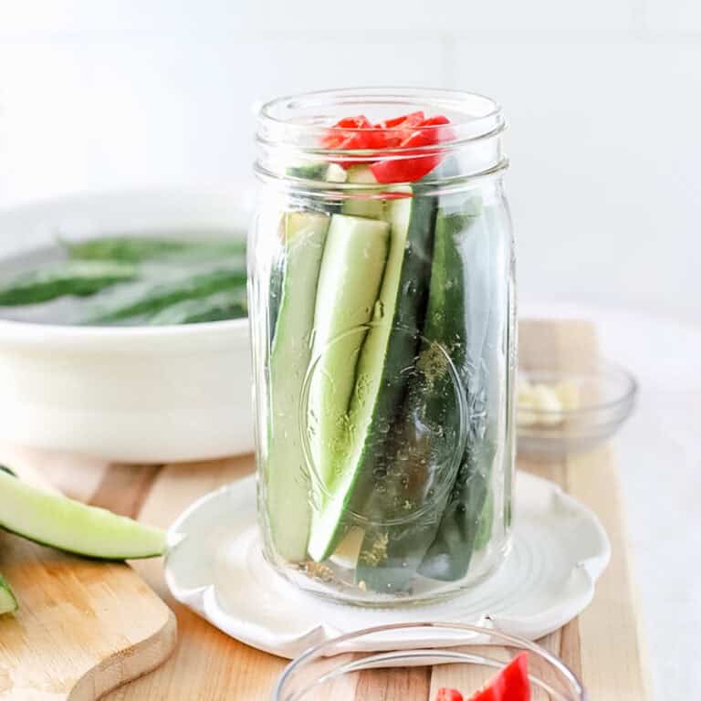 A jar of cucumber pickles that is ready to have the brine poured over and be canned.