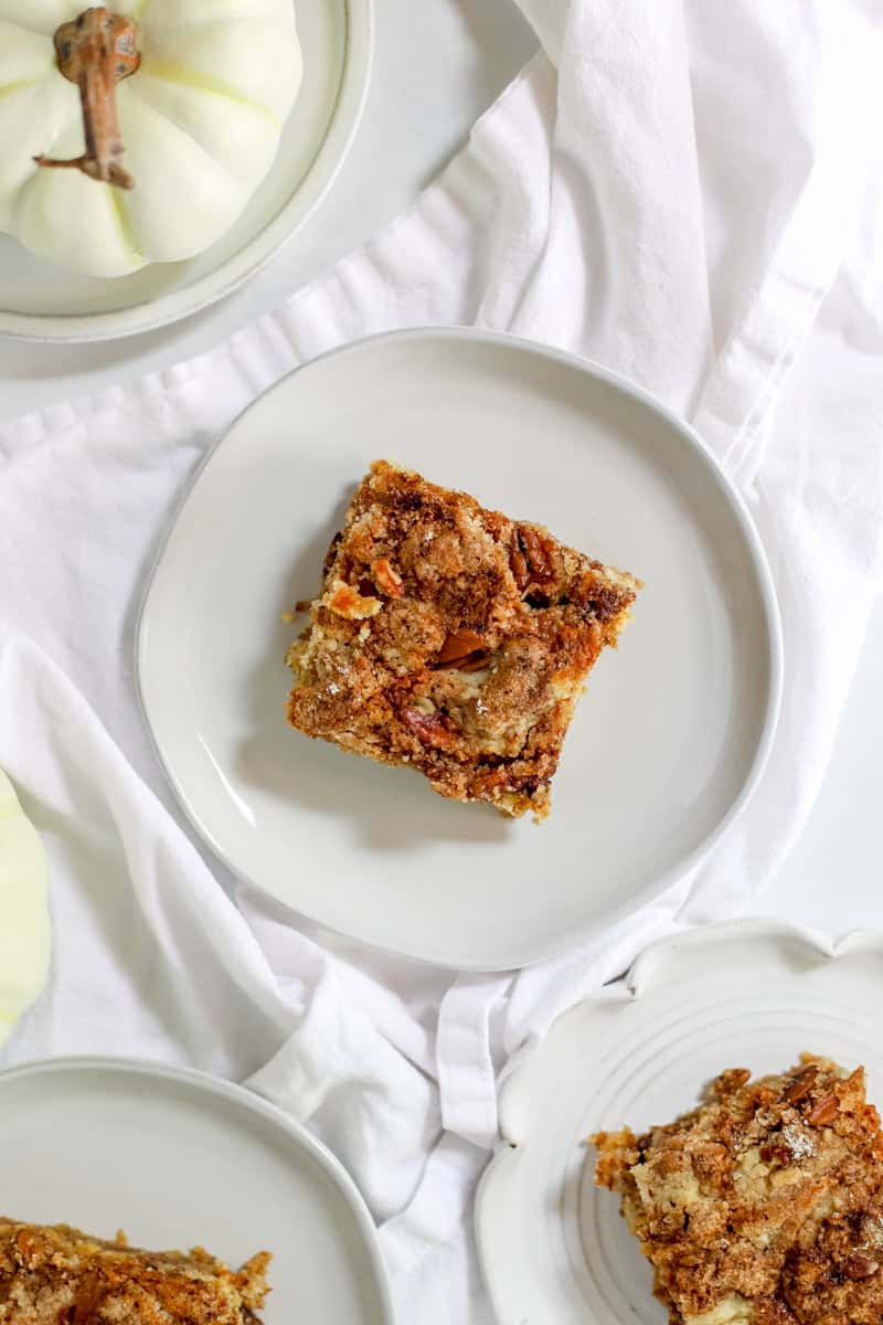 A slice of pumpkin crunch cake no cake mix on a white plate and some little white pumpkins in the background.