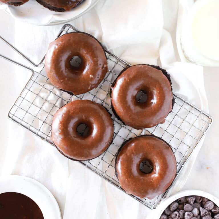 Four chocolate cake donuts on a wire cooling rack.