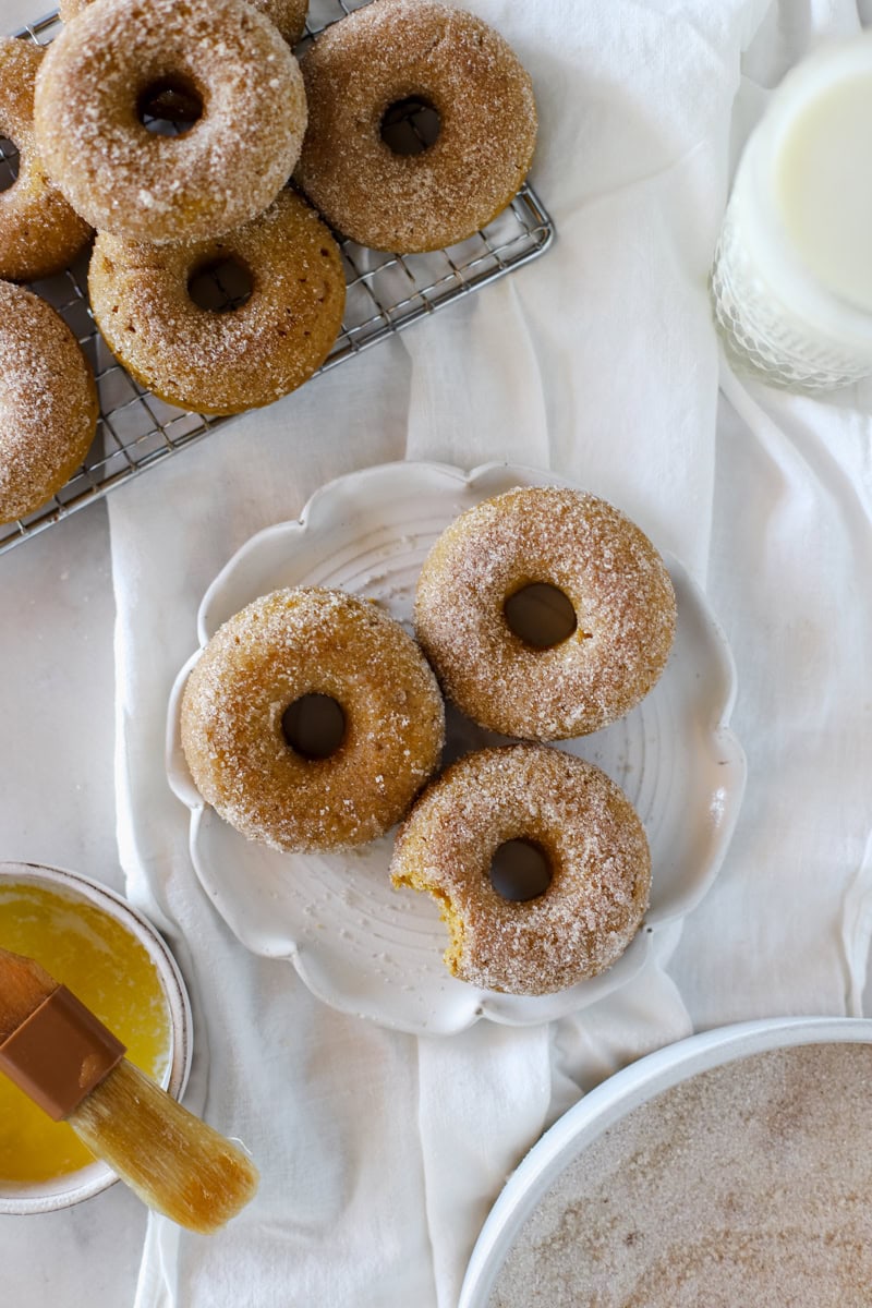 Baked pumpkin spice donuts with cinnamon sugar coating on a white background and plate.
