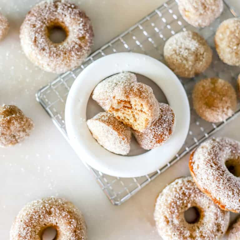 Baked apple cider donut holes on a cooling rack and in a white bowl.