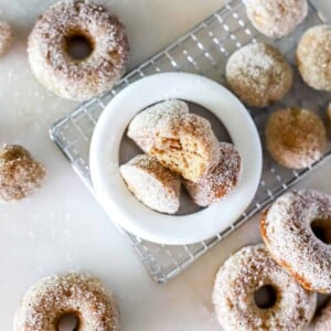 Baked apple cider donut holes on a cooling rack and in a white bowl.