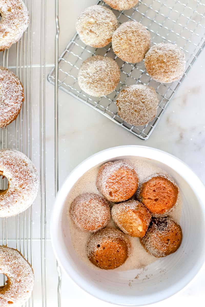 Step 5 of making apple cider donut holes is While the freshly baked donuts are still warm, dip the tops into the cinnamon sugar mixture, coating well.