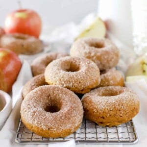 Old-fashioned apple cider donuts on a cooling rack with a few apple slices in the background.