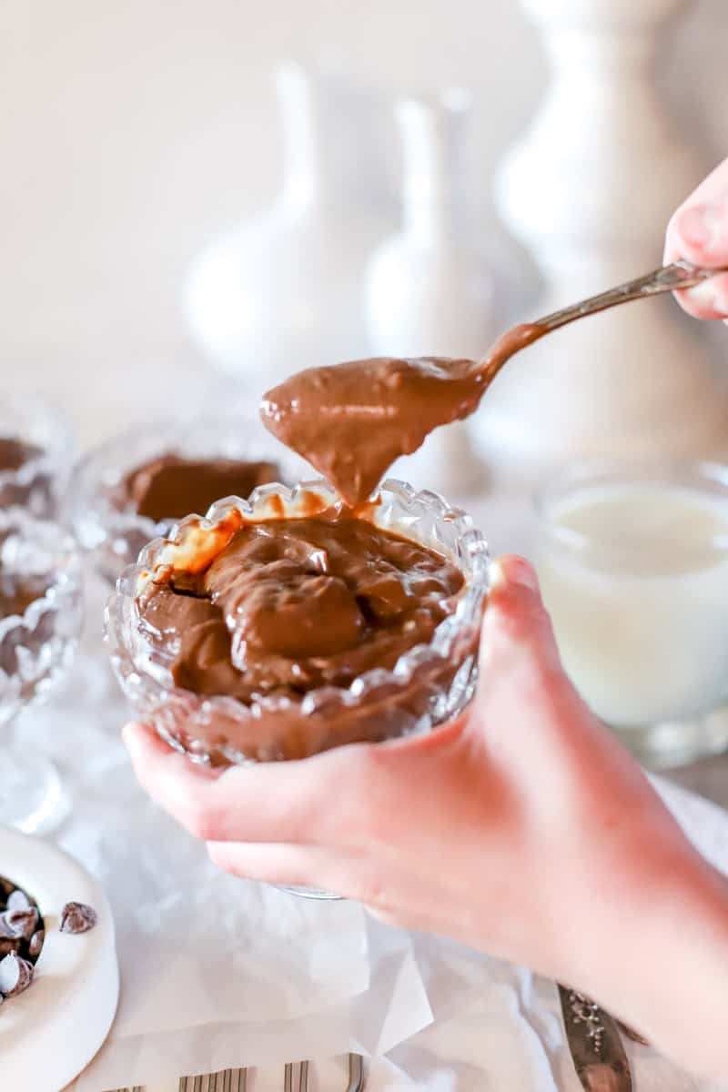 A child's hand holding a glass cup of chocolate pudding.