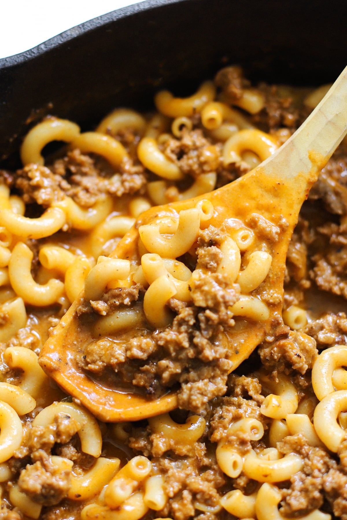 Close-up of creamy venison hamburger helper with tender elbow macaroni and ground deer meat in a cheddar cheese sauce, stirred with a wooden spoon.