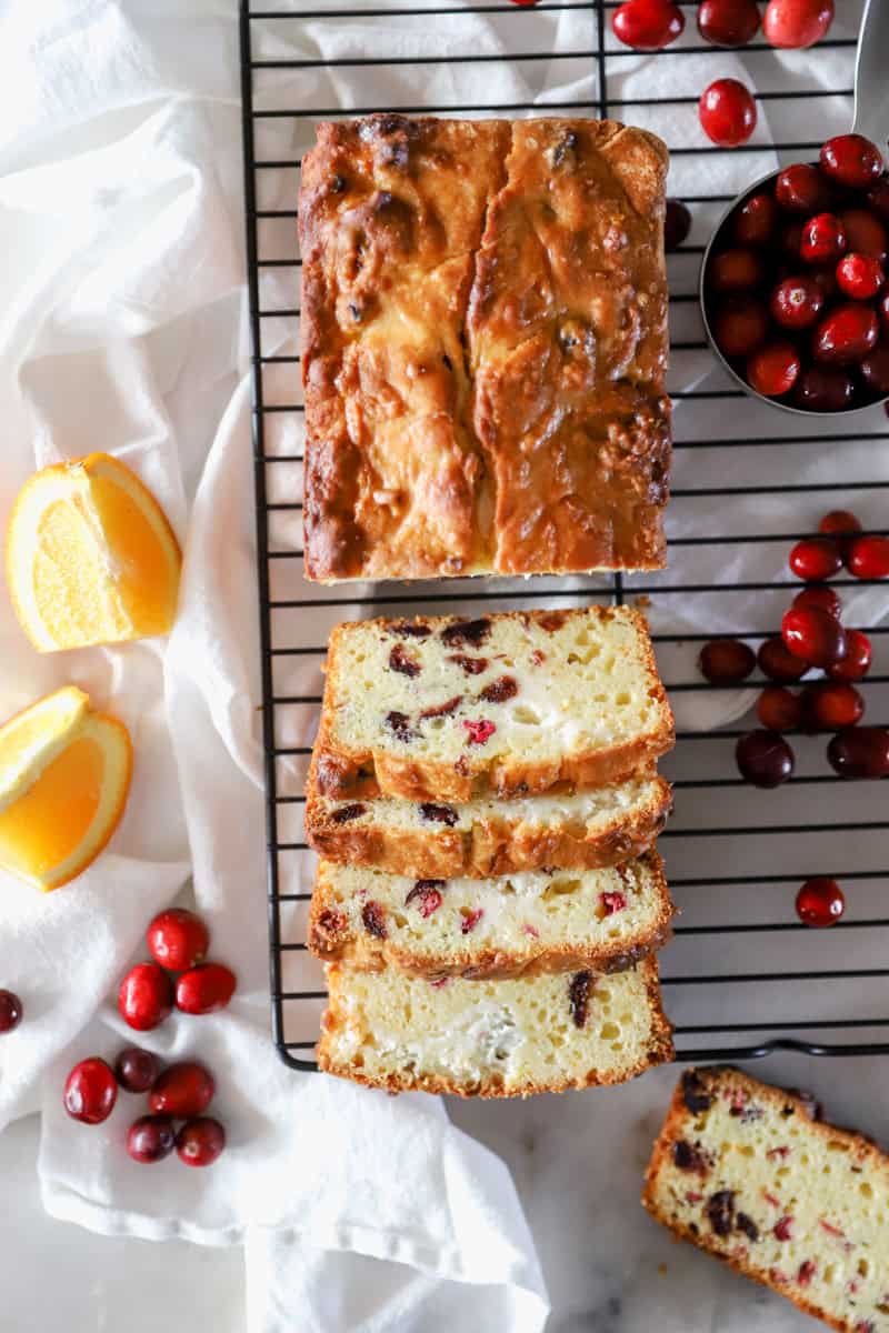 A top view of cranberry cream cheese bread on a cooling rack that has been sliced to show the dried cranberries and orange zest.