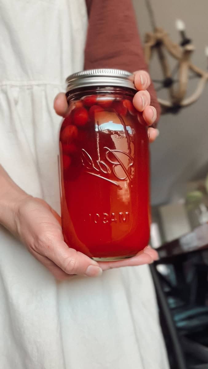 A woman holding a jar of homemade cranberry juice in a mason jar.