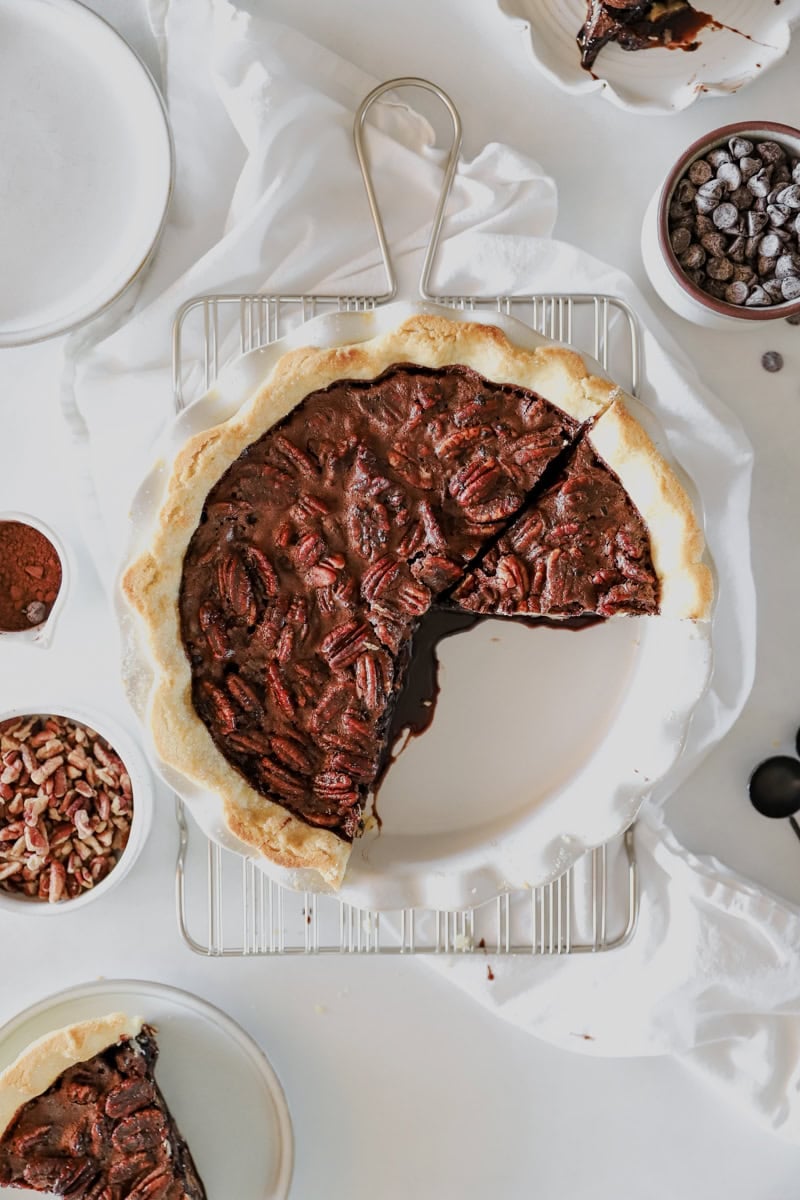 A top view of the ingredients for chocolate pecan pie surrounding a baked pie with a few slices removed.
