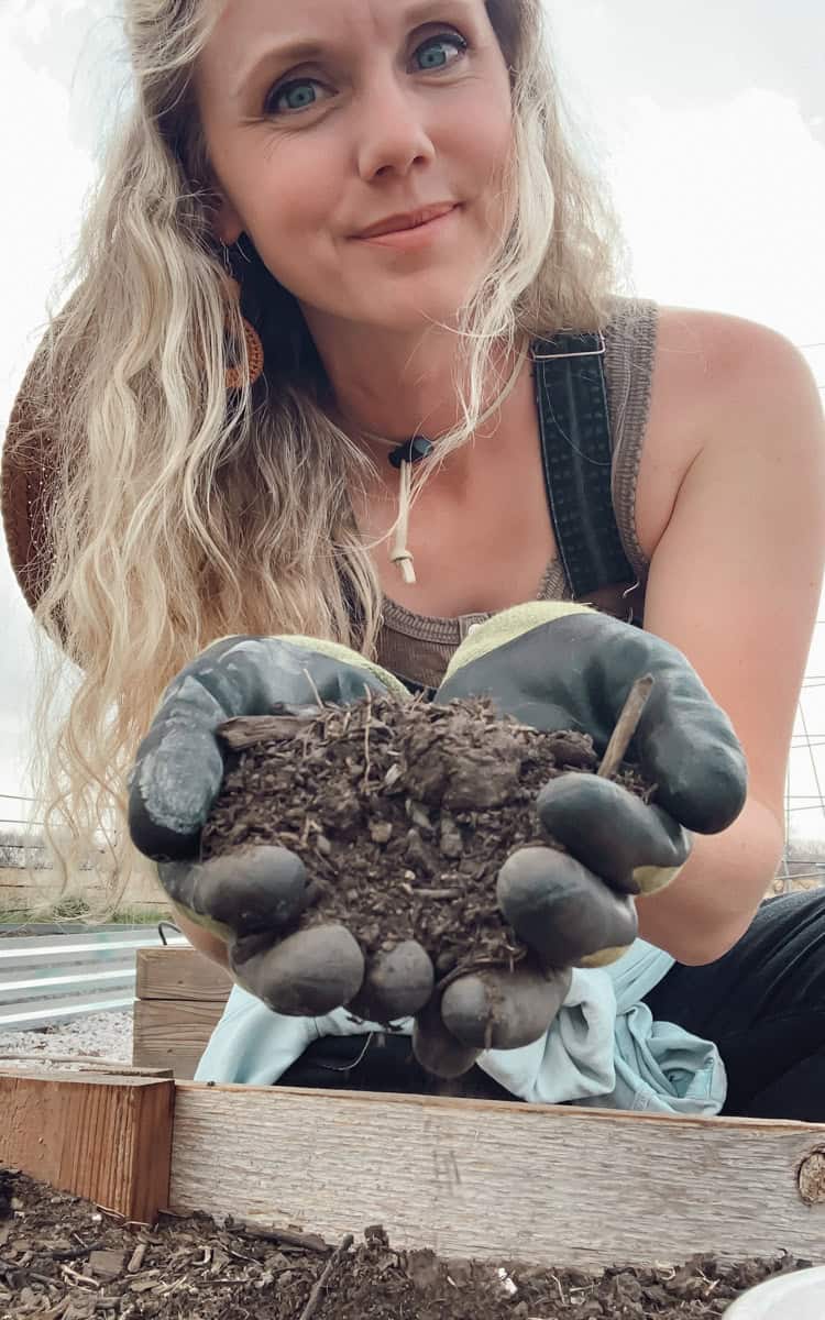Meg from Ninnescah Homestead holding soil in her gardening gloves explaining cheap ways to add nitrogen to the soil.