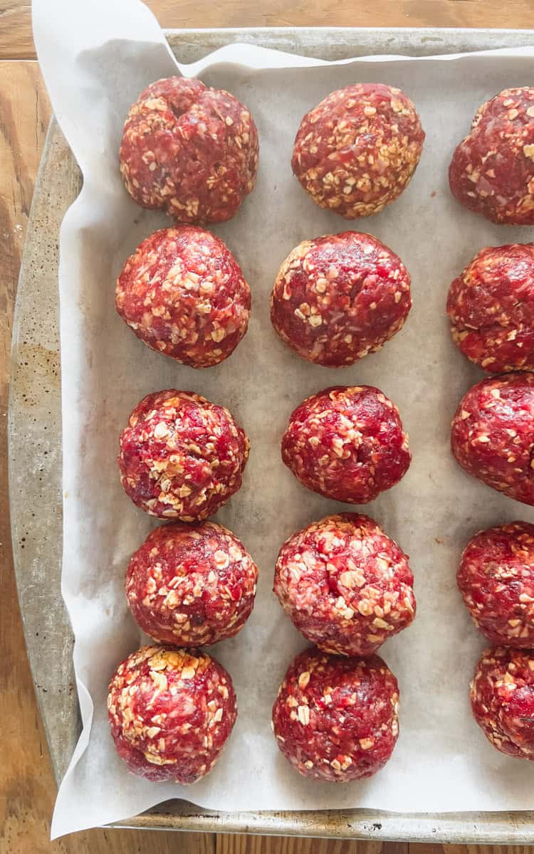 Step two of making venison meatballs is shaping the meat into balls and placing it on a parchment lined baking sheet.