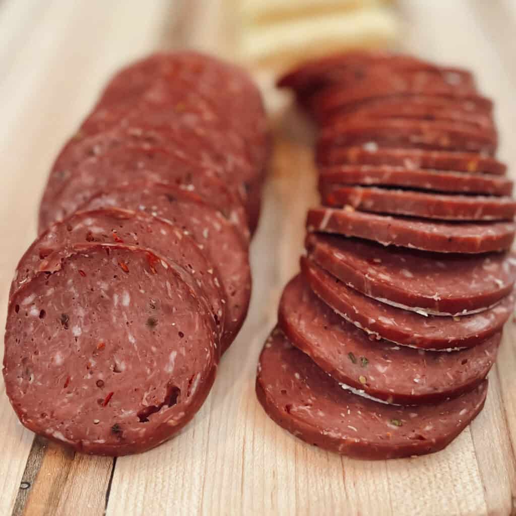 A close up view of deer meat smoked venison summer sausage sliced on a wood board.