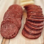 A close up view of deer meat smoked venison summer sausage sliced on a wood board.