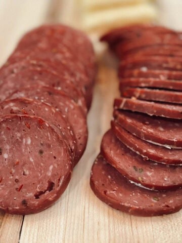 A close up view of deer meat smoked venison summer sausage sliced on a wood board.