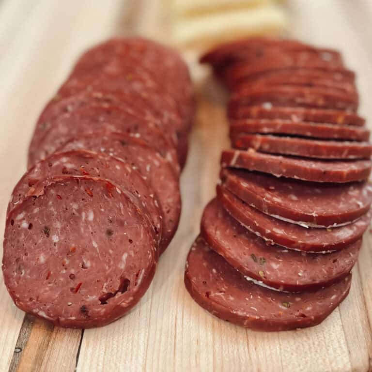 A close up view of deer meat smoked venison summer sausage sliced on a wood board.