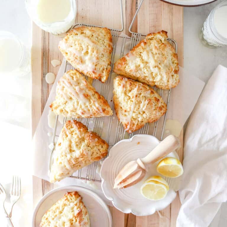 A group of freshly baked lemon sourdough scones made with sourdough discard on a parchment garnished with lemons.