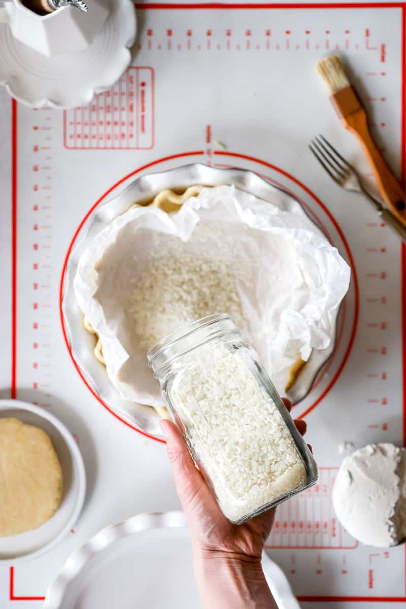 A pie crust lined with parchment paper being filled with rice pie weights for blind baking.
