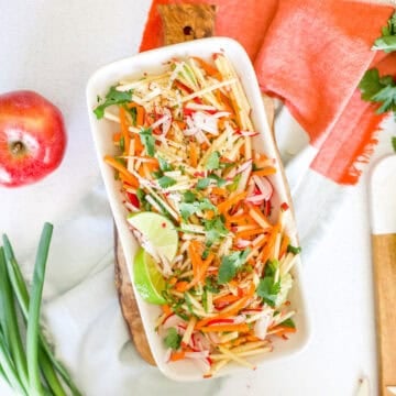 A platter of apple slaw on a brightly colored napkin with apple and scallion garnishes.