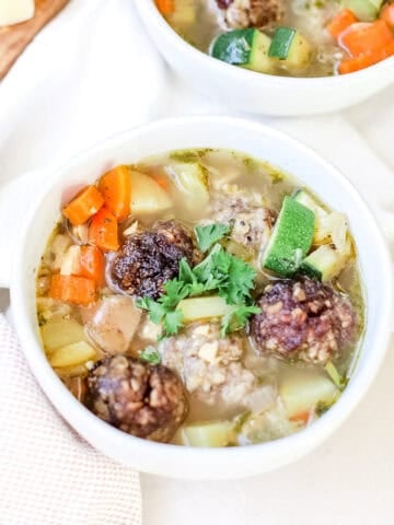 Italian Wedding Soup with Venison Meatballs in white bowls with parsley garnishes.