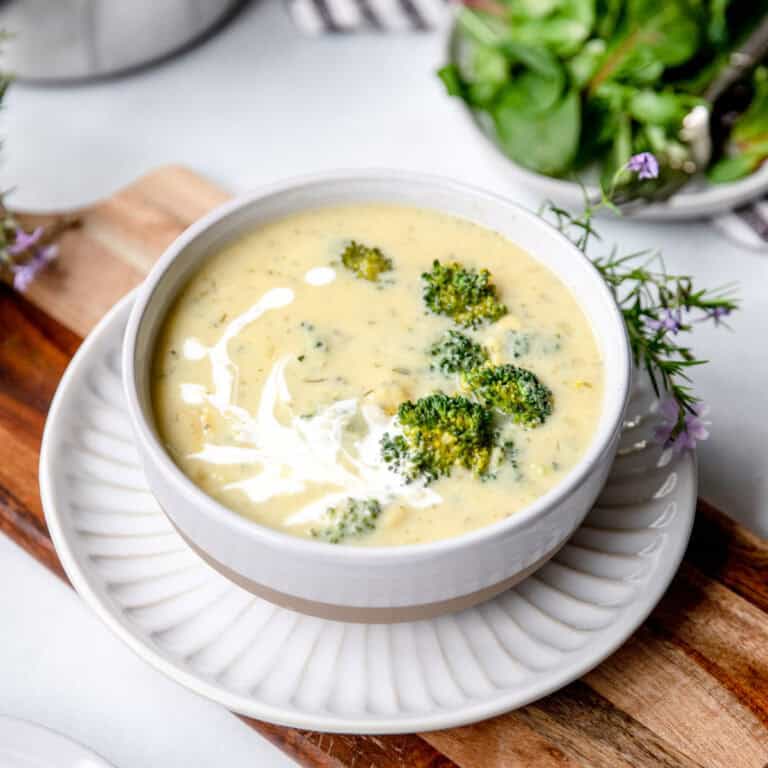 Broccoli and cheddar soup in a white stoneware bowl with a swirl of cream to garnish.