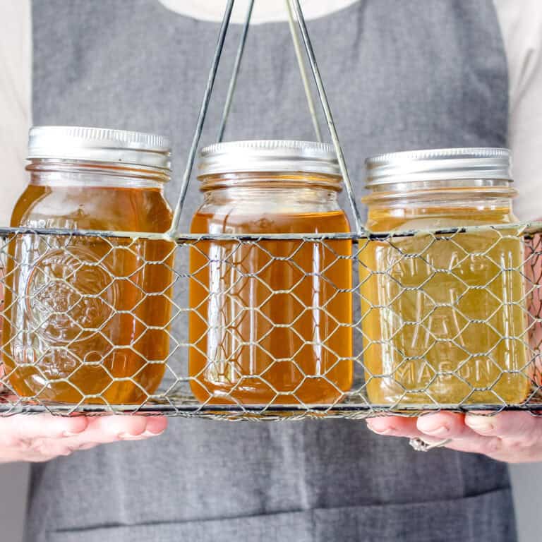 Six mason jars of chicken broth being held by Meg from Ninnescah Homestead.