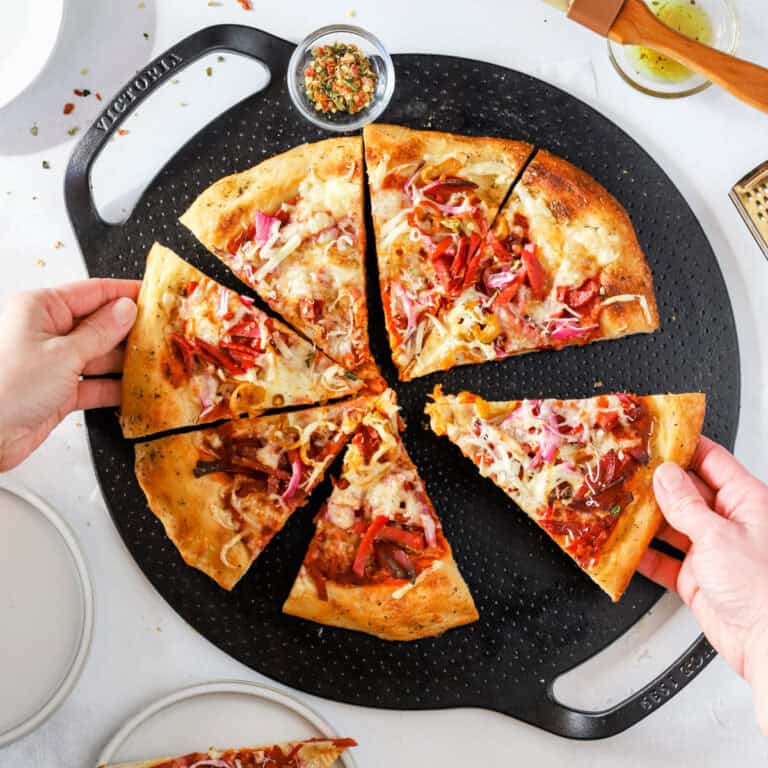 Hands reaching for slices of Italian Grinder Pizza on a Victorria cookware cast iron pizza pan.