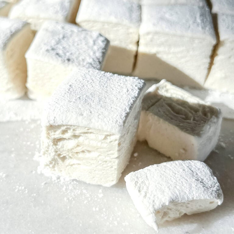 A square-cut homemade marshmallow dusted with powdered sugar showing the air pockets and delicious inside.
