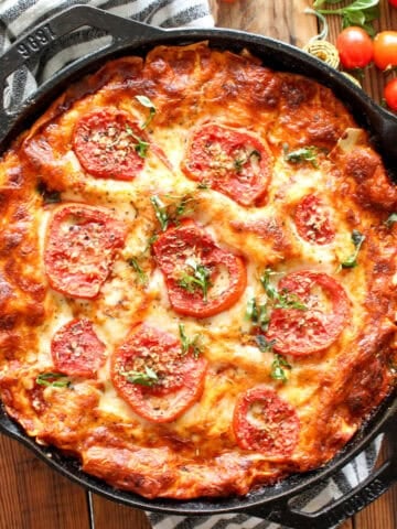A cast-iron skillet lasagna with garden fresh tomatoes on a striped linen.